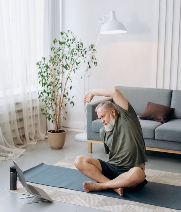 Man stretching peacefully in a bright, sunlit room, embodying a sense of calm and flexibility.